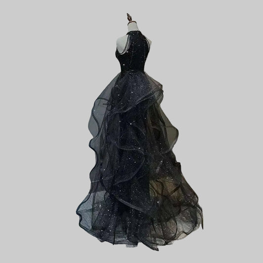 Black evening gown with sheer layers on a mannequin against a gray wall.