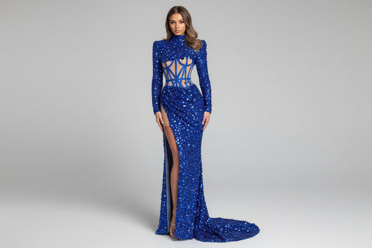 Woman wearing a blue sequin dress with a high slit, standing against a neutral wall.