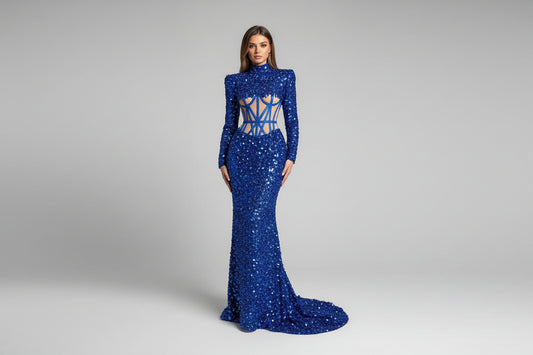 Woman wearing a blue evening gown with a high slit, standing against a neutral wall.