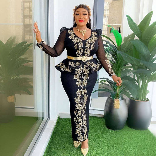 Woman in a black outfit with gold embroidery standing indoors with plants.